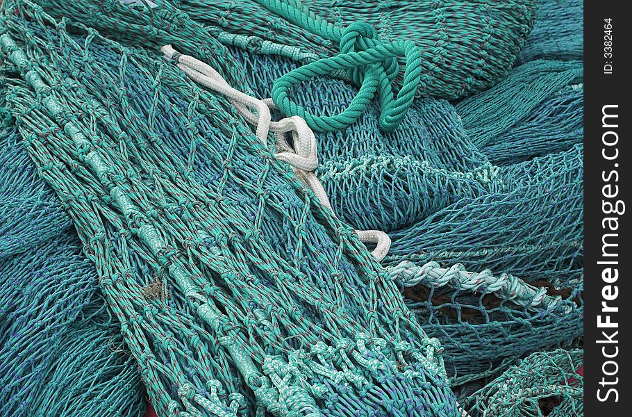 Blue and Green trawler nets piled on the quayside at a busy fishing port. Blue and Green trawler nets piled on the quayside at a busy fishing port.