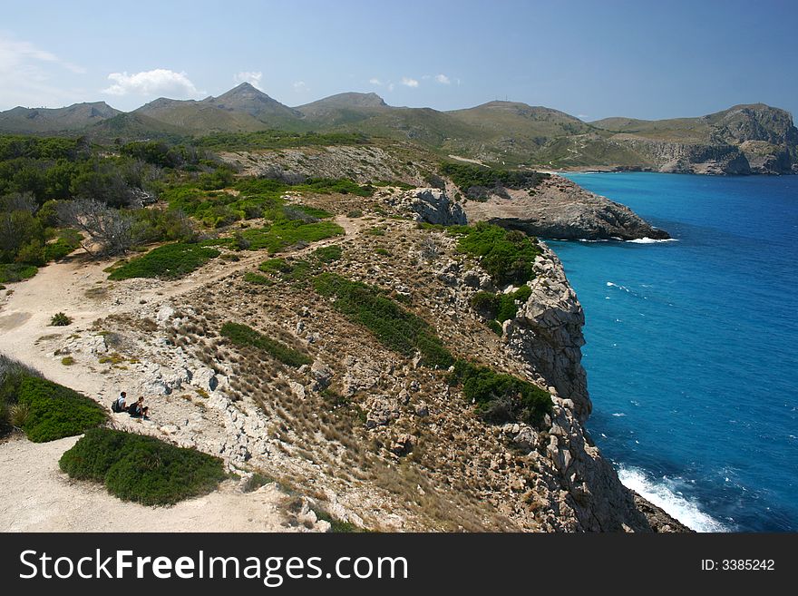 Two wanderers sitting at the coast of Majorca watching the beautiful blue mediterranean sea resting before going on on their path. Two wanderers sitting at the coast of Majorca watching the beautiful blue mediterranean sea resting before going on on their path