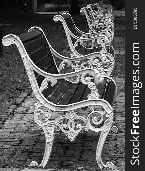 A row of park benches made from ornately decorated iron and wood, leading the eye to infinity