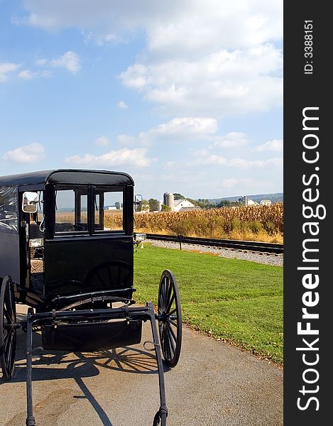 A close up view of the front of an authentic Amish horse-drawn buggy or wagon beside a railroad track with an Amish farm and cornfield in the background. Lancaster County, Pennsylvania (USA)