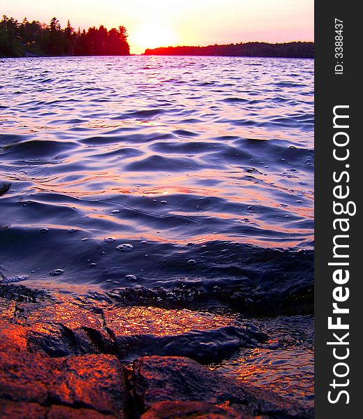 The Sun Sets over a Lake with a Rocky Shore. The Sun Sets over a Lake with a Rocky Shore