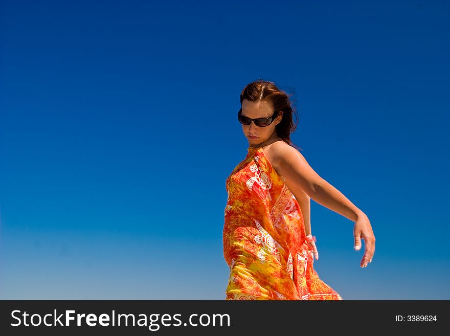 View from side of woman standing on the beach wearning orange pareo placed on the sky. View from side of woman standing on the beach wearning orange pareo placed on the sky