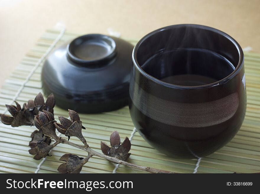 Black cup of tea with steam on brown background