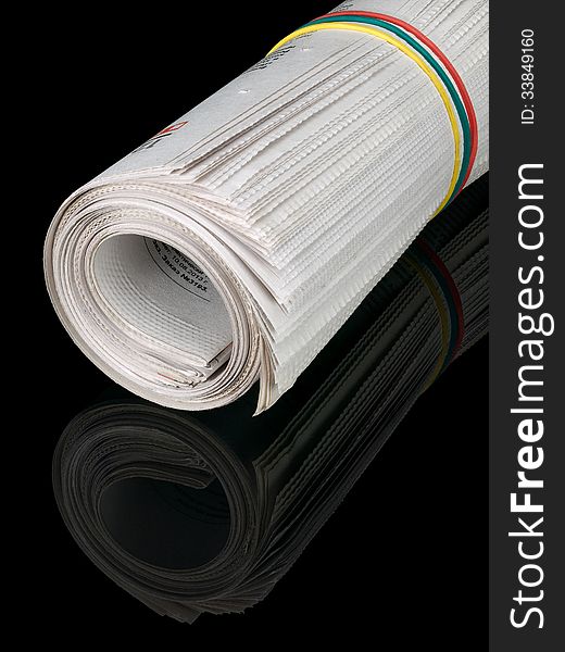 The roll of the newspapers which have been pulled together with an elastic band on a black background. The roll of the newspapers which have been pulled together with an elastic band on a black background