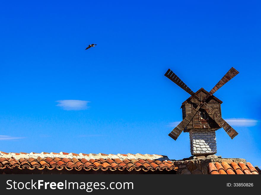 Decorative windmill installed at the Architecture building on a background of the clear sky with a flying seagull. Decorative windmill installed at the Architecture building on a background of the clear sky with a flying seagull