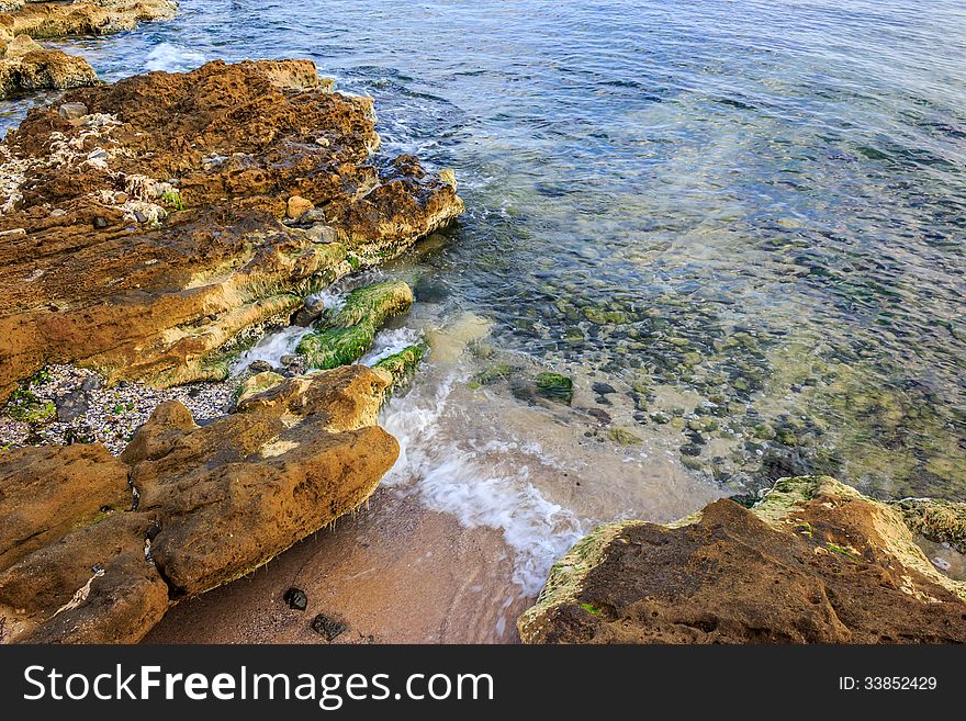 Ocean waves breaking on a rocky shore. through the water can be seen seabed. pebbles, shells and seaweed lie on the seabed. Ocean waves breaking on a rocky shore. through the water can be seen seabed. pebbles, shells and seaweed lie on the seabed