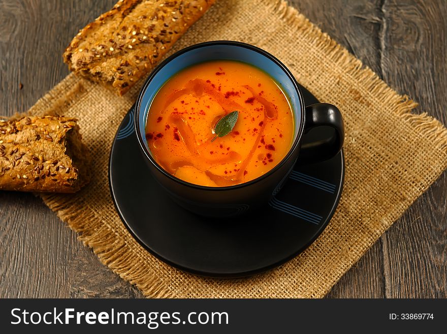Bowl of pumpkin soup with bread on rustic table