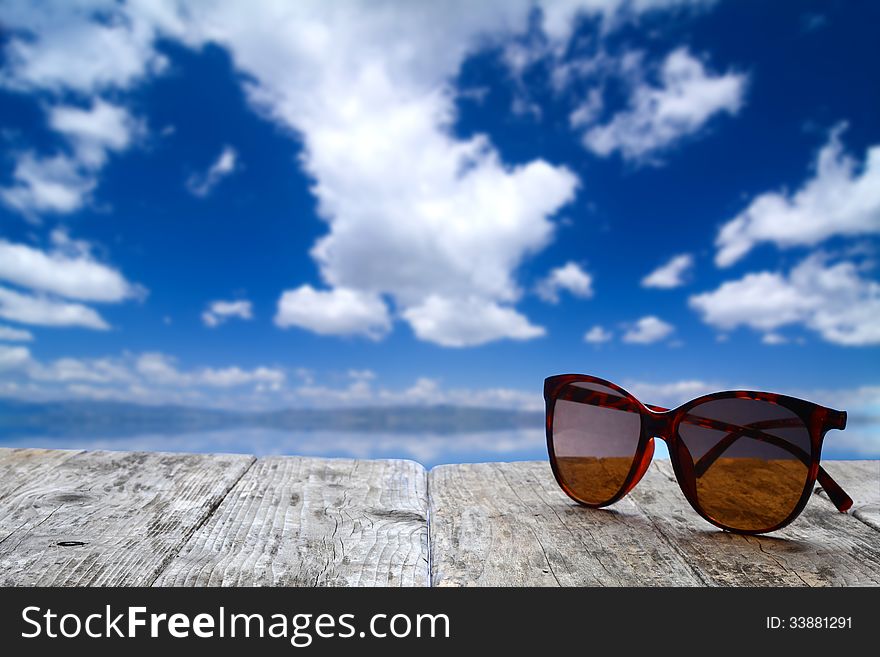 Sun glasses on a wooden surface on a bright sunny day with blue sky and clouds. Sun glasses on a wooden surface on a bright sunny day with blue sky and clouds
