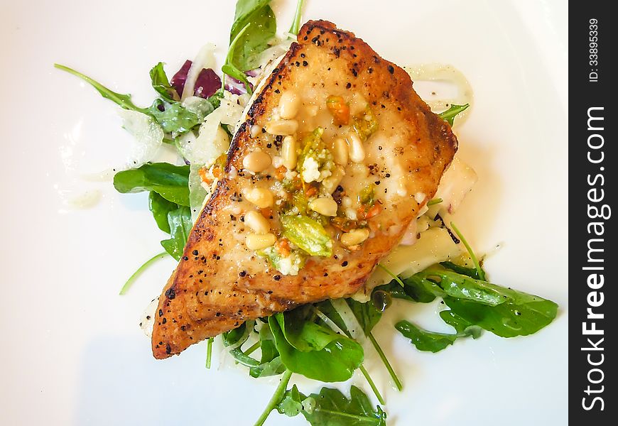 Closeup of fresh pan seared halibut with mixed greens and pine nuts