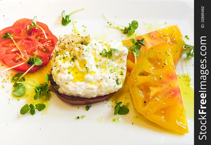 Closeup of heirloom tomatoes with fresh Burrata cheese drizzled with Trampetti olive oil served on a white plate as an appetizer. Closeup of heirloom tomatoes with fresh Burrata cheese drizzled with Trampetti olive oil served on a white plate as an appetizer.