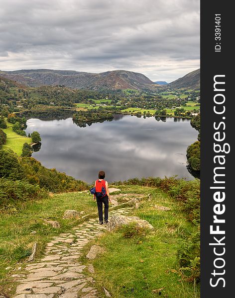 A female hiker descending the path from Loughrigg with Grasmere in the background. A female hiker descending the path from Loughrigg with Grasmere in the background