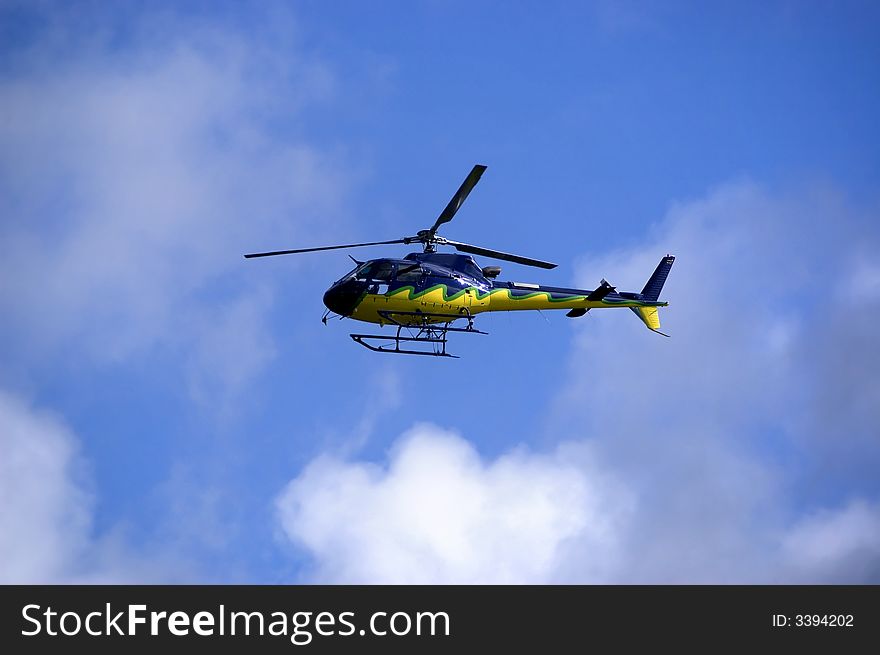 Yellow-blue Helicopter in the sky flying high. Side view. Yellow-blue Helicopter in the sky flying high. Side view.