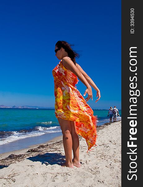 View from side of woman standing on the beach wearning only in orange pareo. View from side of woman standing on the beach wearning only in orange pareo