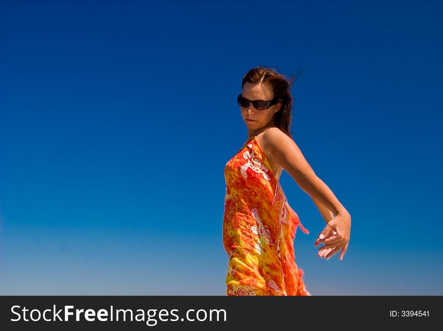 View from side of woman standing on the beach wearning orange pareo placed on the sky. View from side of woman standing on the beach wearning orange pareo placed on the sky