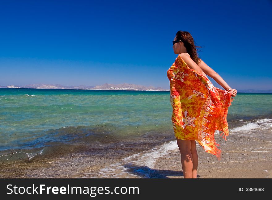 View from side of woman standing on the beach wearning orange pareo placed on the sky. View from side of woman standing on the beach wearning orange pareo placed on the sky