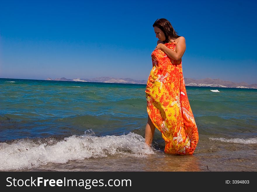 View from side of woman standing on the beach wearning orange pareo placed on the sky. View from side of woman standing on the beach wearning orange pareo placed on the sky