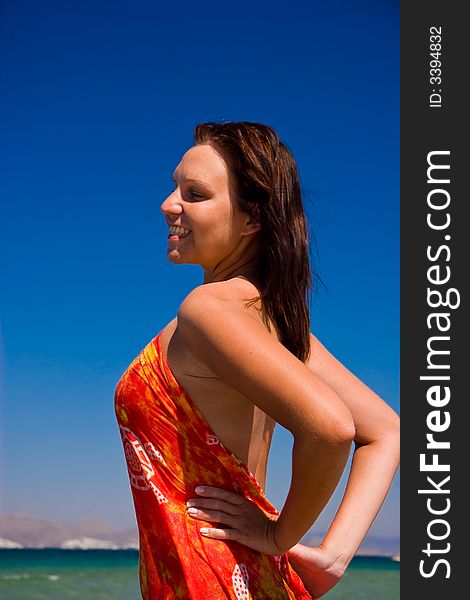 View from side of woman standing on the beach wearning orange pareo placed on the sky. View from side of woman standing on the beach wearning orange pareo placed on the sky