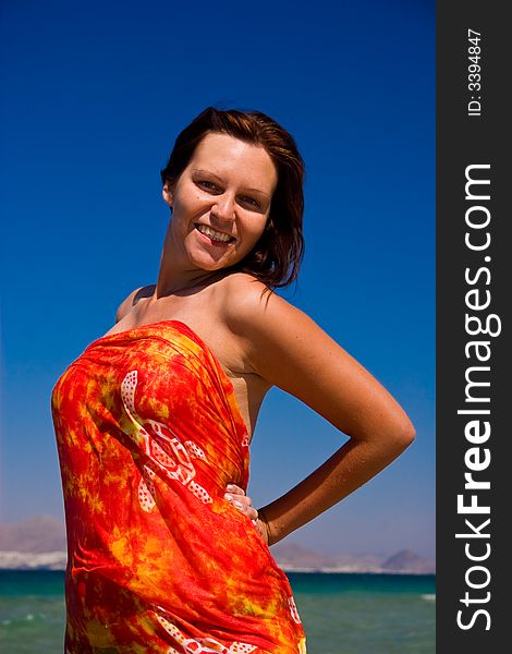 View from side of woman standing on the beach wearning orange pareo placed on the sky. View from side of woman standing on the beach wearning orange pareo placed on the sky