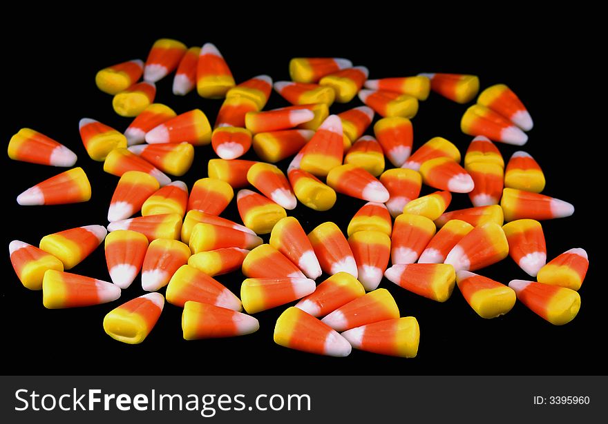 A pile of orange, white and yellow candy corn against a black background.