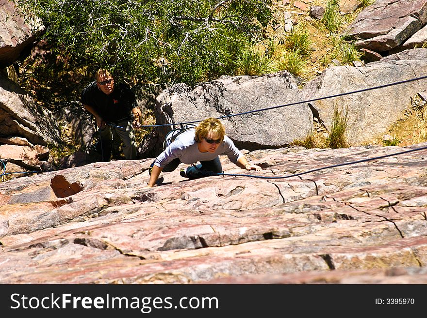 A climber begins her ascent while her belayer stands watch below. A climber begins her ascent while her belayer stands watch below