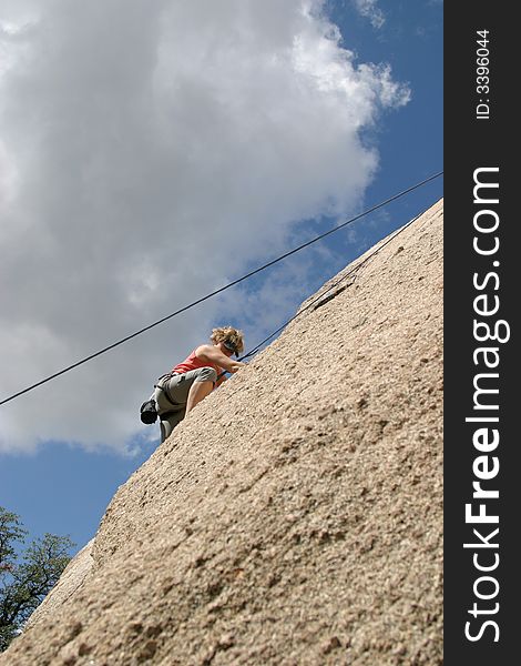 Climber ascending a granite rock with blue skies and clouds behind her. Climber ascending a granite rock with blue skies and clouds behind her.