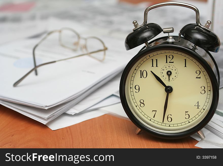 Black alarm clock on a table where other documents lay. Black alarm clock on a table where other documents lay