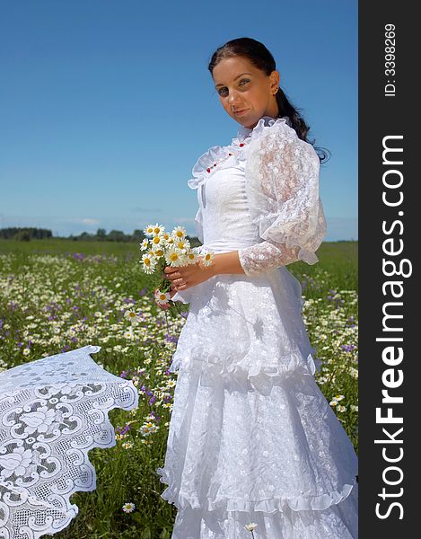 Beautiful young woman, in a white dress under a white umbrella with camomiles, in a field