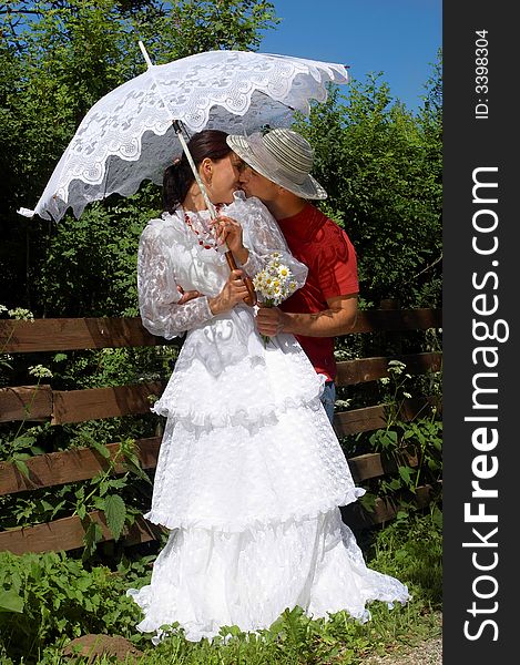 Young happy kissing couple in a sunny day near a fence