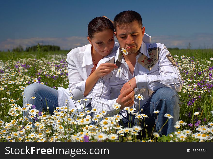 Young happy couple at the sunny day in a field with camomiles and handbells