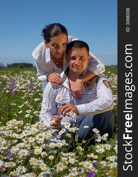 Young happy couple at the sunny day in a field with camomiles and handbells