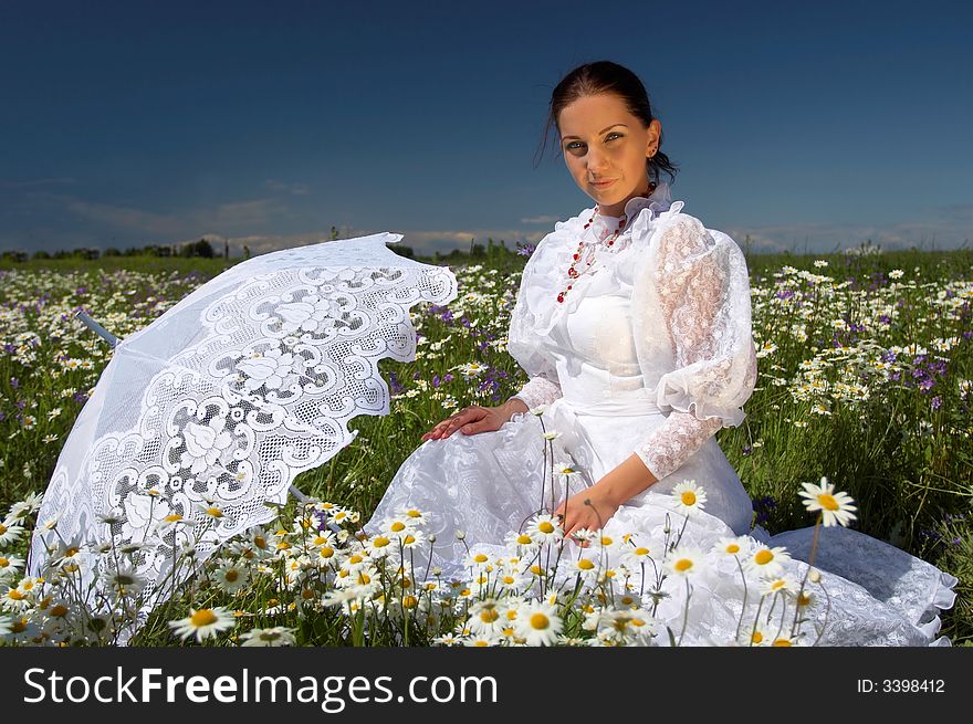 Beautiful young woman, in a white dress under a white umbrella with camomiles, in a field