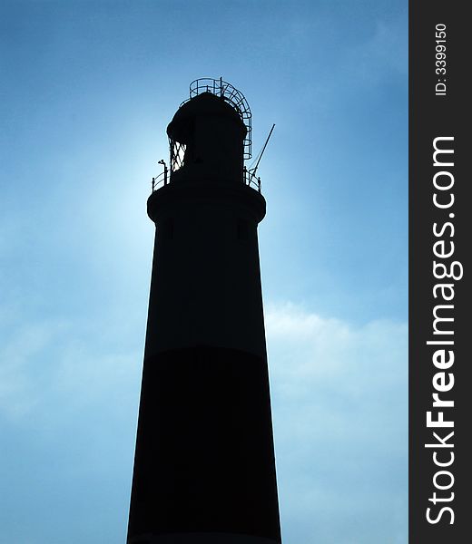 Looking up at Portland Bill Lighthouse, Dorset, England, silhouetted against blue sky.