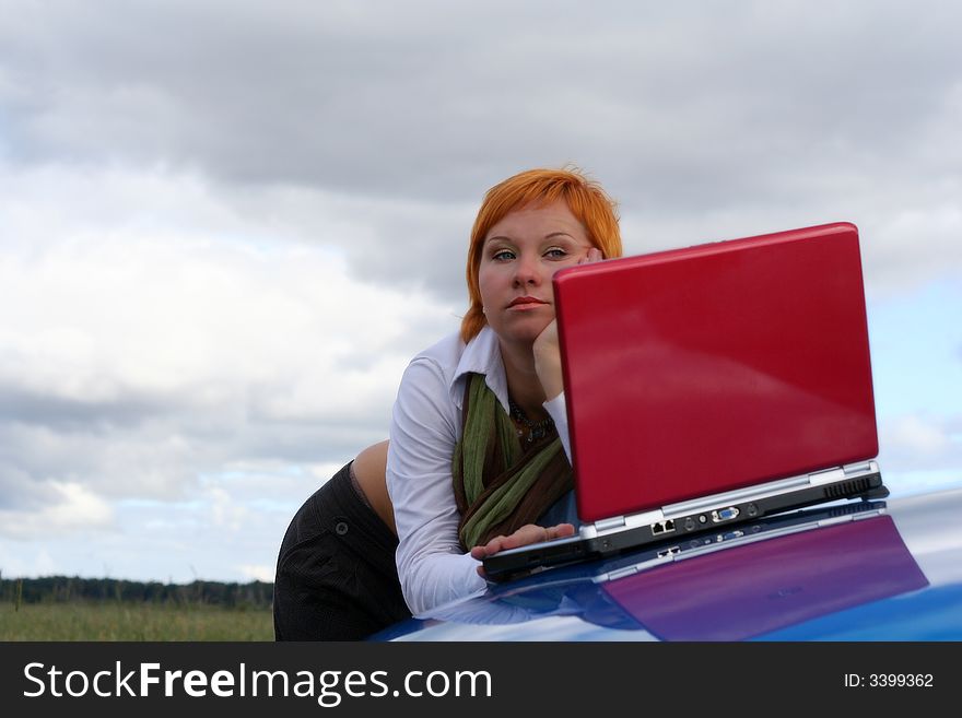Young woman with red notebook on cowl of blue car