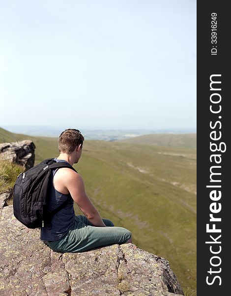 Young man sitting on the rop of the high cliff in mountains, back view. Young man sitting on the rop of the high cliff in mountains, back view