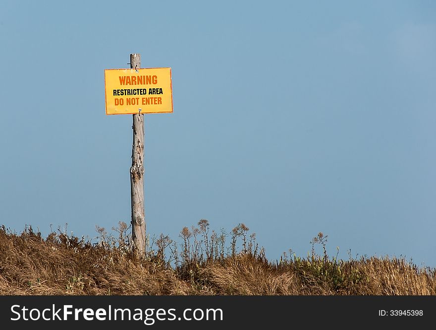 Forbidden territory - a warning sign saying the danger. Yellow sign on the pole at the blue sky background - Warning, Restricted area, Do not enter.