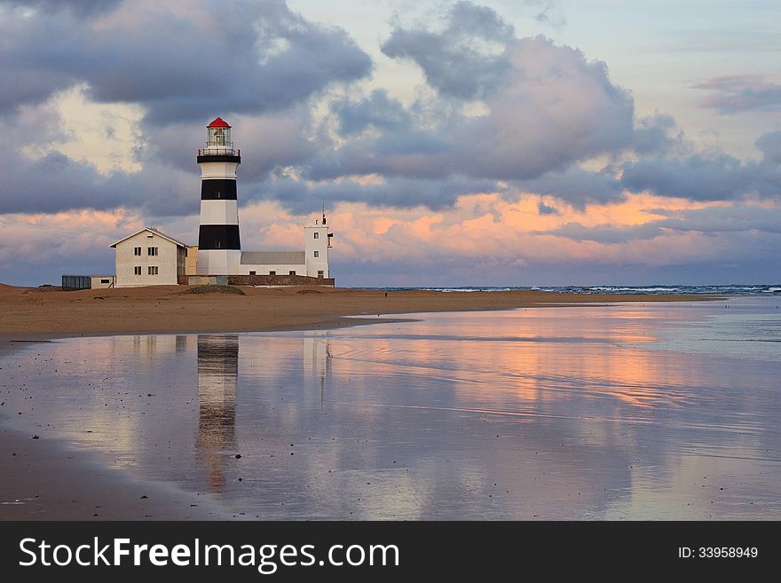 Sunset at beach on South African east coast with lighthouse reflected in sea water. Sunset at beach on South African east coast with lighthouse reflected in sea water