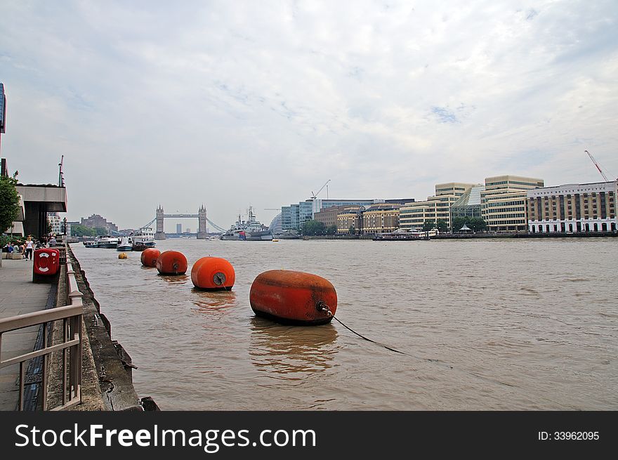Tower Bridge in the background looking up the river Thames with floating orange buoys in the fore ground and hms Belfast in the background. Tower Bridge in the background looking up the river Thames with floating orange buoys in the fore ground and hms Belfast in the background