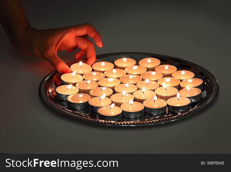 A hand takes candle from a tray with lots of burning candles. A hand takes candle from a tray with lots of burning candles