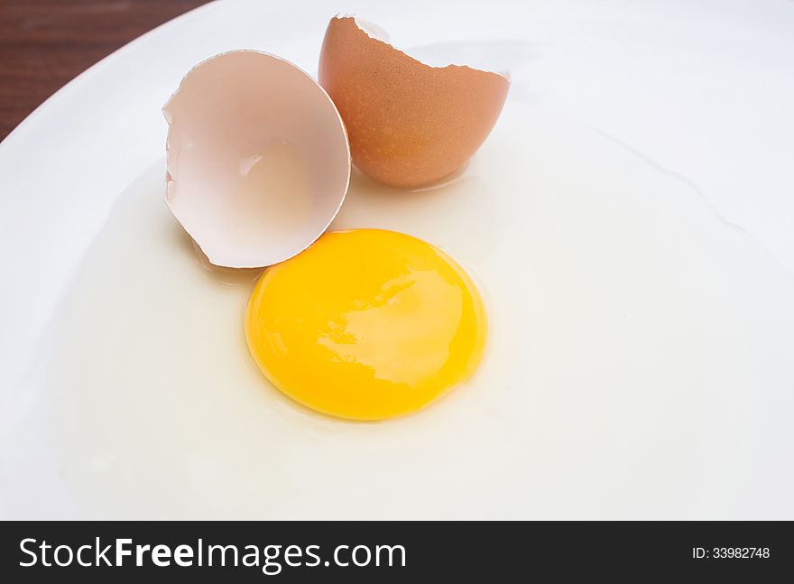 Cracked chicken egg with yolk and egg shell on dish background. Cracked chicken egg with yolk and egg shell on dish background.