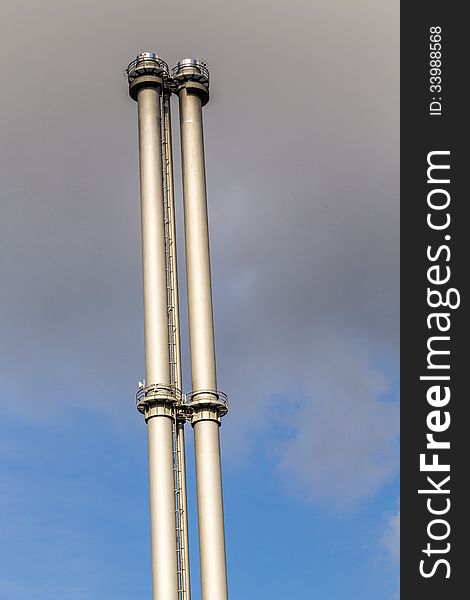 Two metal chimneys against the blue sky with dark clouds