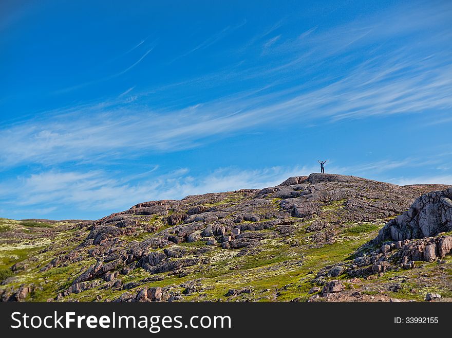 Man with a backpack on a mountain spread wide his hands in the summer against a blue sky with clouds