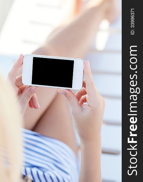 Girl in a bathing suit lying on a white chaise lounge with touch phone