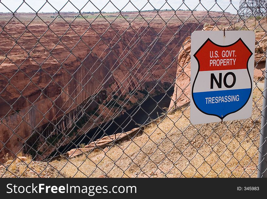A bright red, white and blue sign on a chain link fence keeps citizens out of scenic red sandstone canyons and the cliffs near Glen Canyon Dam in Arizona. A bright red, white and blue sign on a chain link fence keeps citizens out of scenic red sandstone canyons and the cliffs near Glen Canyon Dam in Arizona