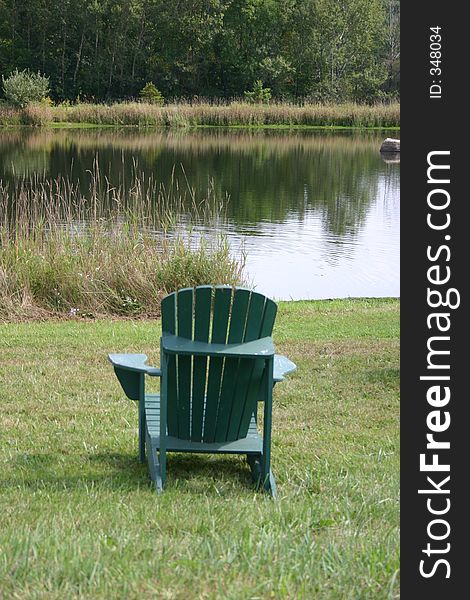 A worn green beach chair sitting in the lawn at a pond. A worn green beach chair sitting in the lawn at a pond.