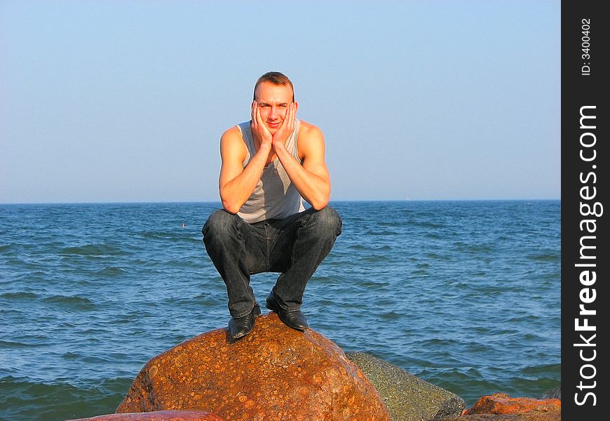 Handsome young man sitting on an old stone on the sea shore. Handsome young man sitting on an old stone on the sea shore