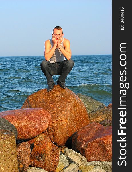 Handsome young man sitting on an old stone on the sea shore. Handsome young man sitting on an old stone on the sea shore