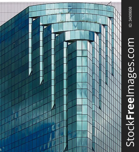 Modern skycraper with a notched sloping corner and covered with blue glass panels which reflects the sky. Modern skycraper with a notched sloping corner and covered with blue glass panels which reflects the sky.