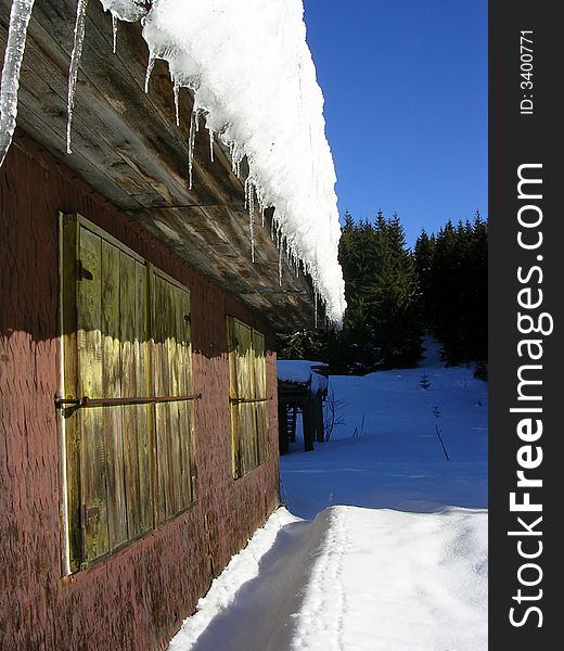 Wooden cottage in mountains weigh in to snow with icicles