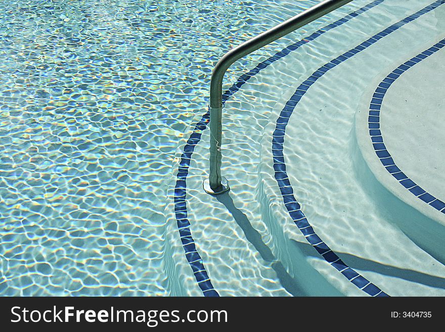 Swimming pool steps and rail with the rippling warm blue waters