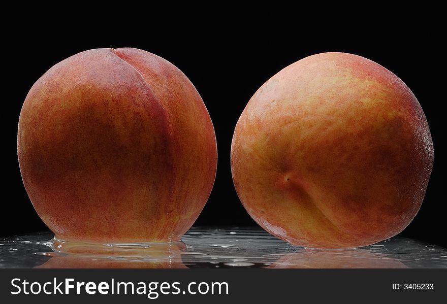 Two wet peaches over black background